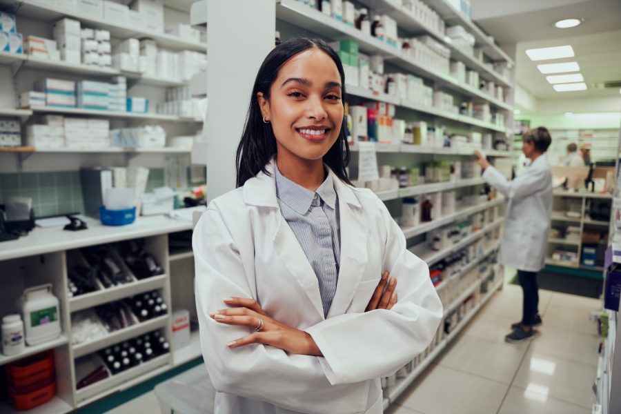 Portrait of young pharmacist standing between aisle in chemist with colleague