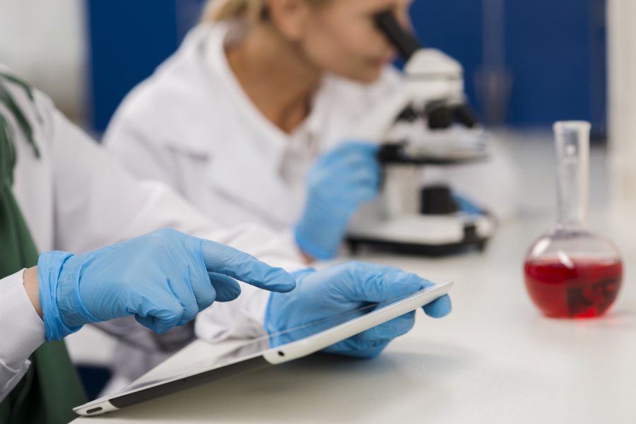 side-view-female-scientists-lab-working-with-microscope-tablet